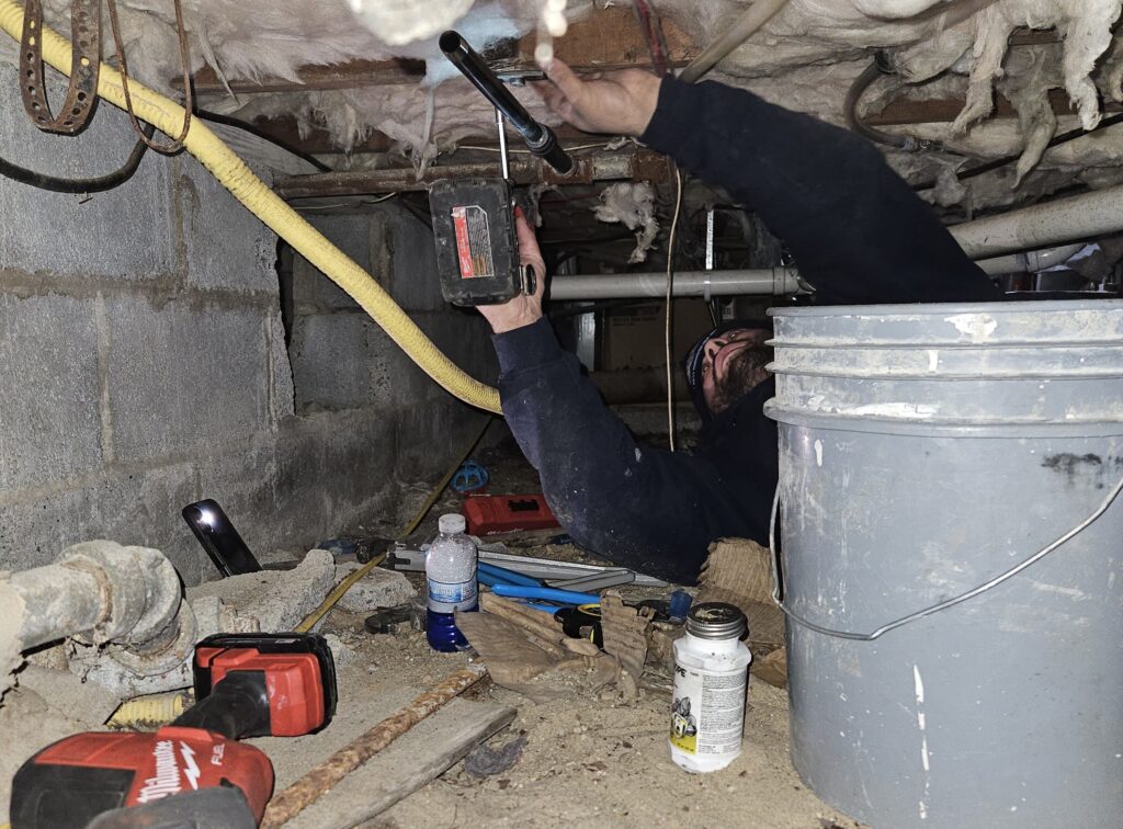 Plumber laying on his back using tools to fix pipe in crawlspace
