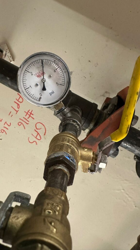 Gas pressure gauge reading 3 PSI on a labeled shutoff valve, Ariel Service Inc, next to apartment marker #1116.