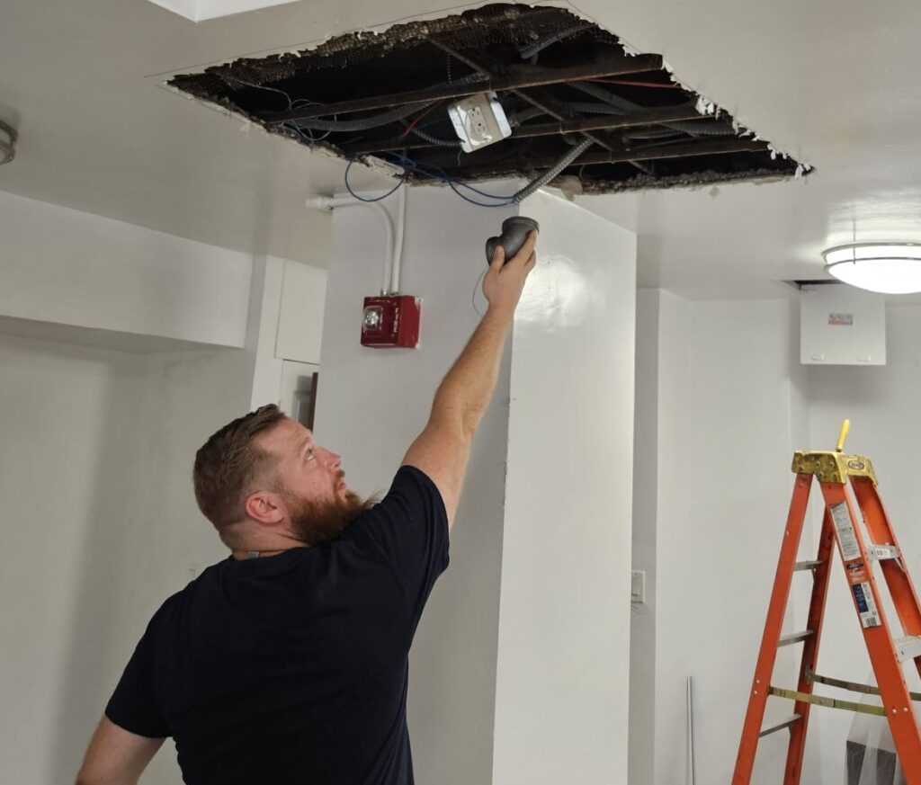 Ariel Services, Inc. Plumber holding pipe elbow, repairing gas piping in ceiling