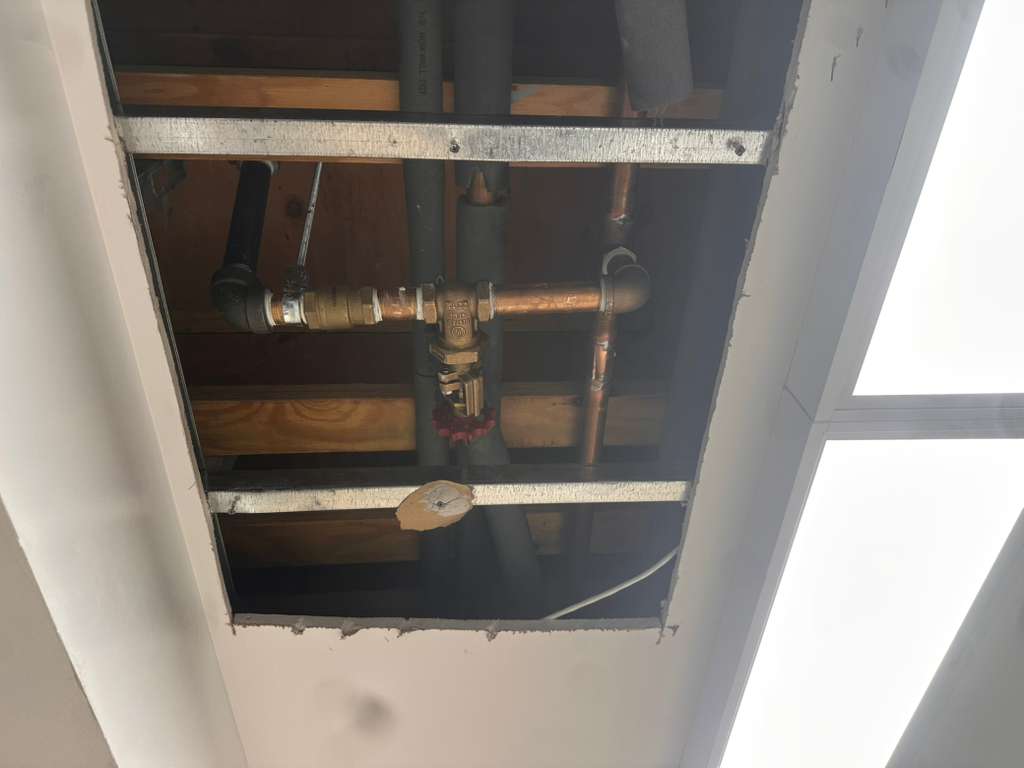 Exposed ceiling cavity showing copper piping and a shutoff valve, Ariel Service Inc, between wood joists during a repair.