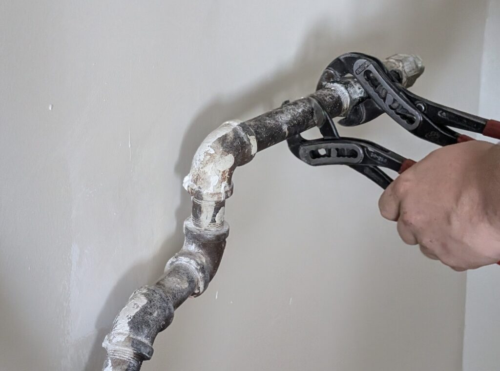 Ariel Services plumber using 2 channel locks to remove old gas piping to be replaced