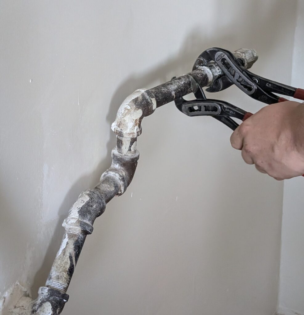 Ariel Services plumber using 2 channel locks to remove old gas piping to be replaced